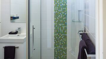Une salle de bain moderne avec une douche à parois de verre, un lavabo blanc et une serviette violette posée sur un porte-serviettes.