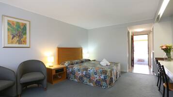 A hotel room with a bed, a desk, a chair, a nightstand, and a painting on the wall.