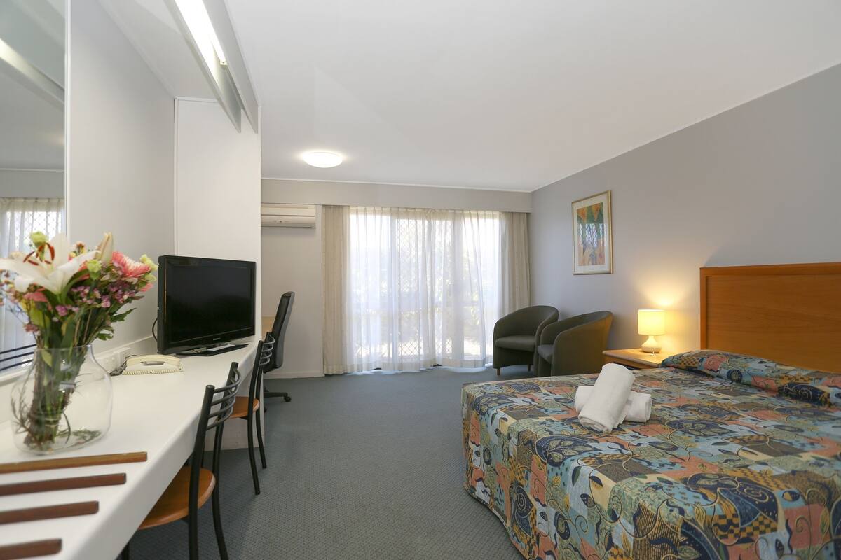 Hotelkamer met een bed, een bureau met een computer, een stoel, een televisie en een raam met gordijnen.