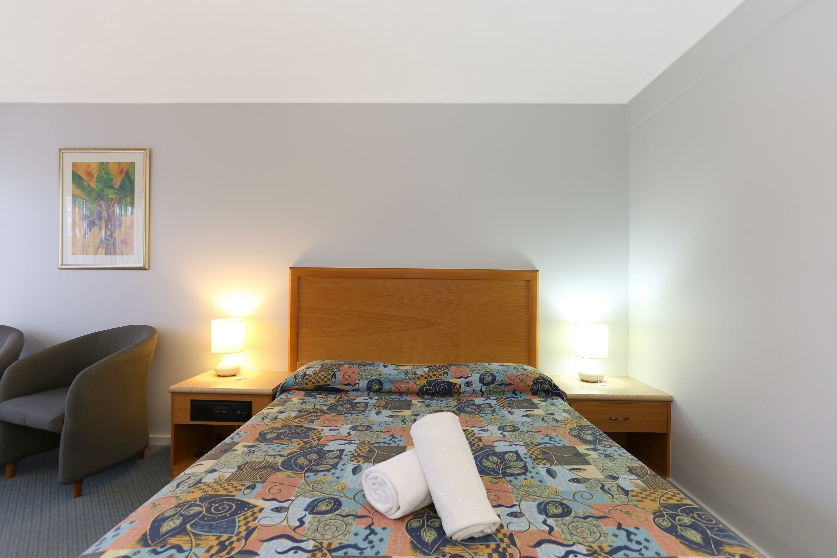 A hotel room with a bed, two bedside tables, a chair, and a wall-mounted painting.