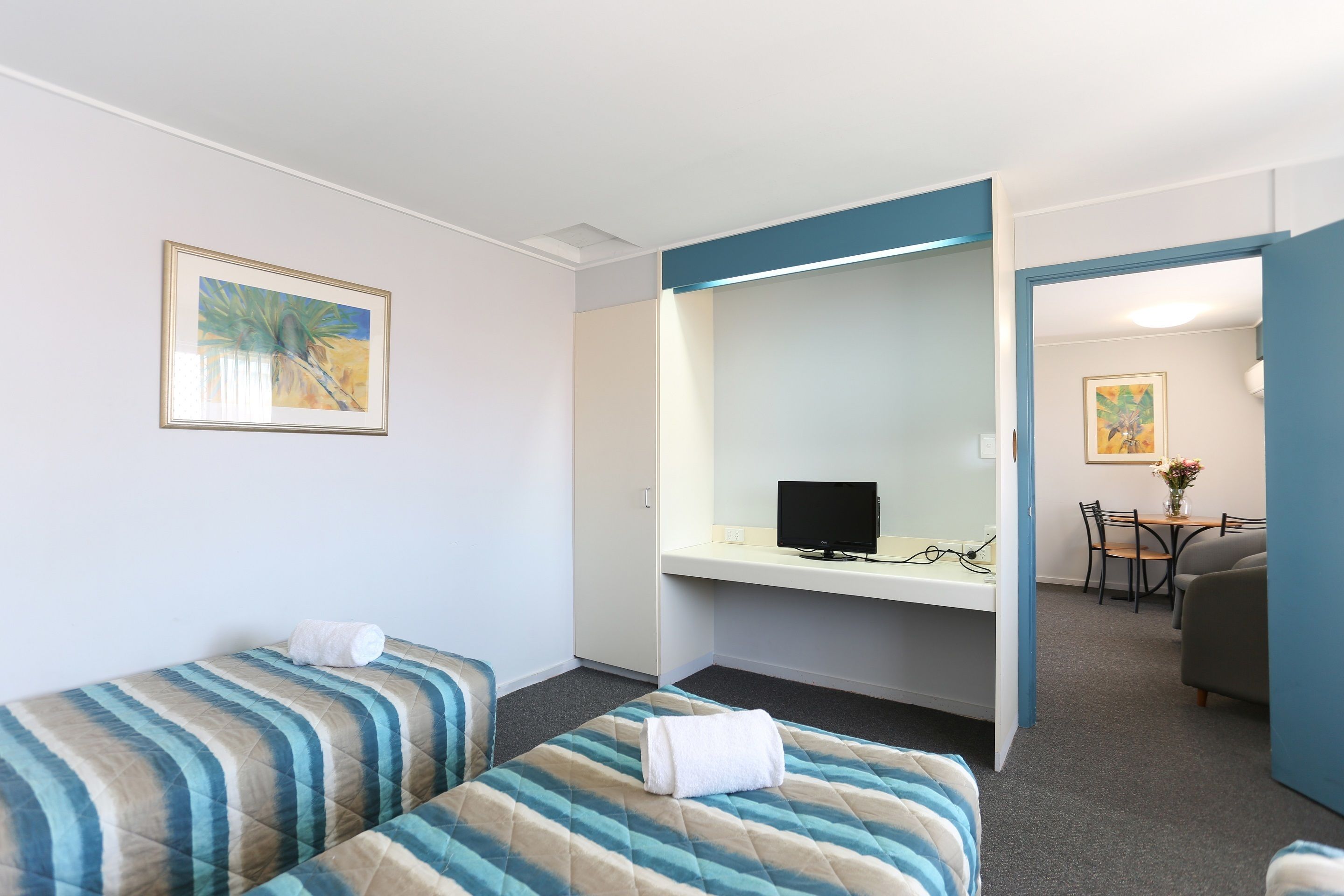 A hotel room with two beds, a desk with a computer, a chair, and a dining area with a table and chairs.