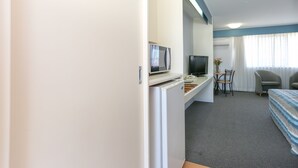 Quarto de hotel com cama, escrivaninha com computador e televisão, uma cadeira e janela com cortinas.