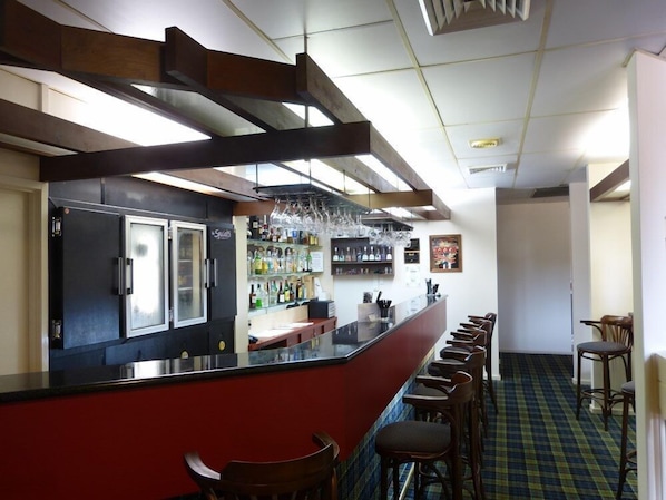 A bar area with a counter, stools, and a refrigerator.