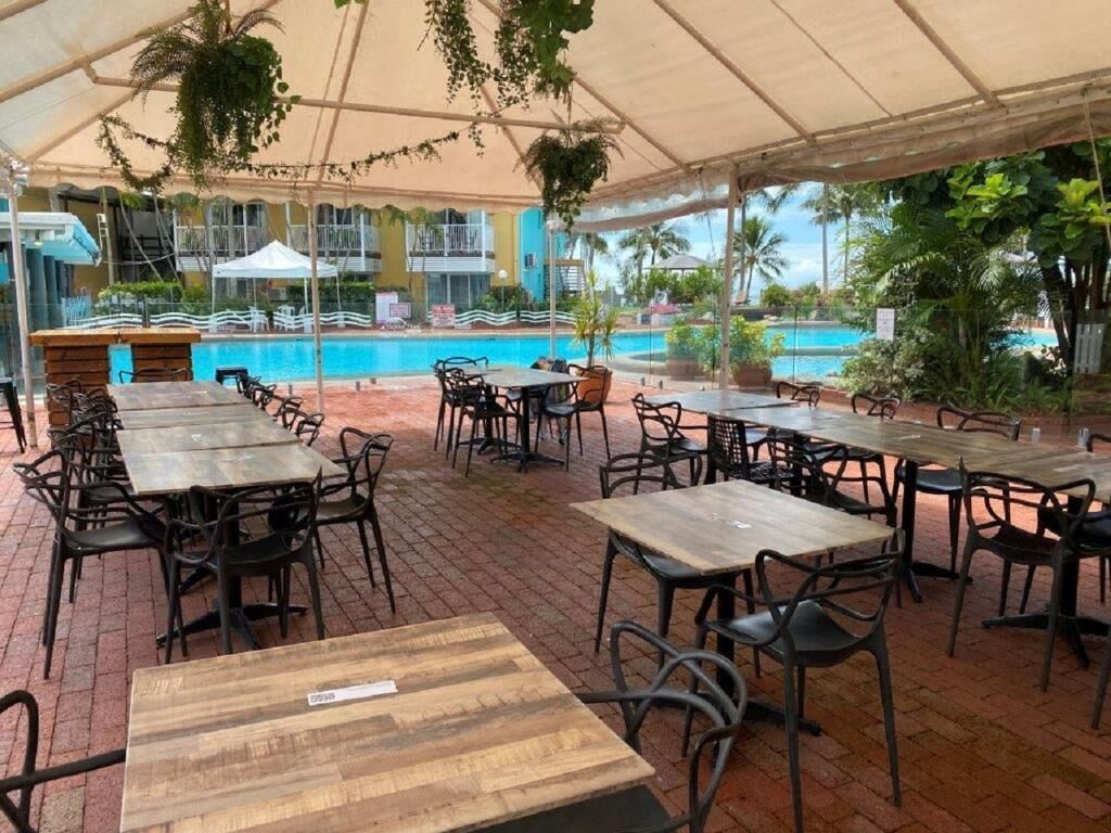 Un espace extérieur aménagé pour les repas, avec des tables et des chaises, une piscine en arrière-plan et une terrasse couverte.