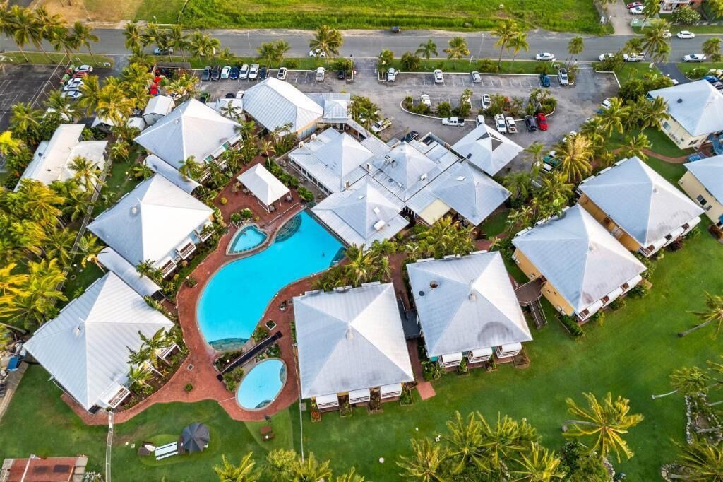 A resort with multiple bungalow-style buildings, a central swimming pool, and surrounding palm trees.