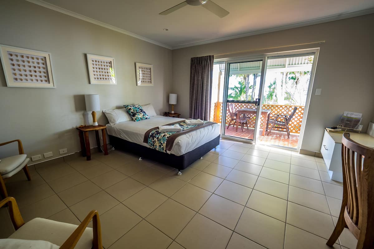 Habitación de hotel con cama, escritorio, silla, balcón con vistas y ventilador de techo.