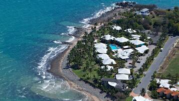 An aerial view of a coastal property with a beach, a swimming pool, and multiple white-roofed buildings.