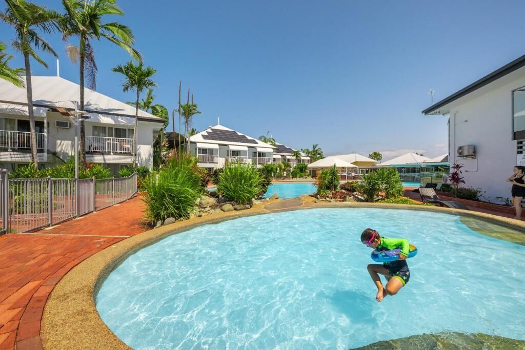 A swimming pool with a person diving, surrounded by palm trees and buildings.
