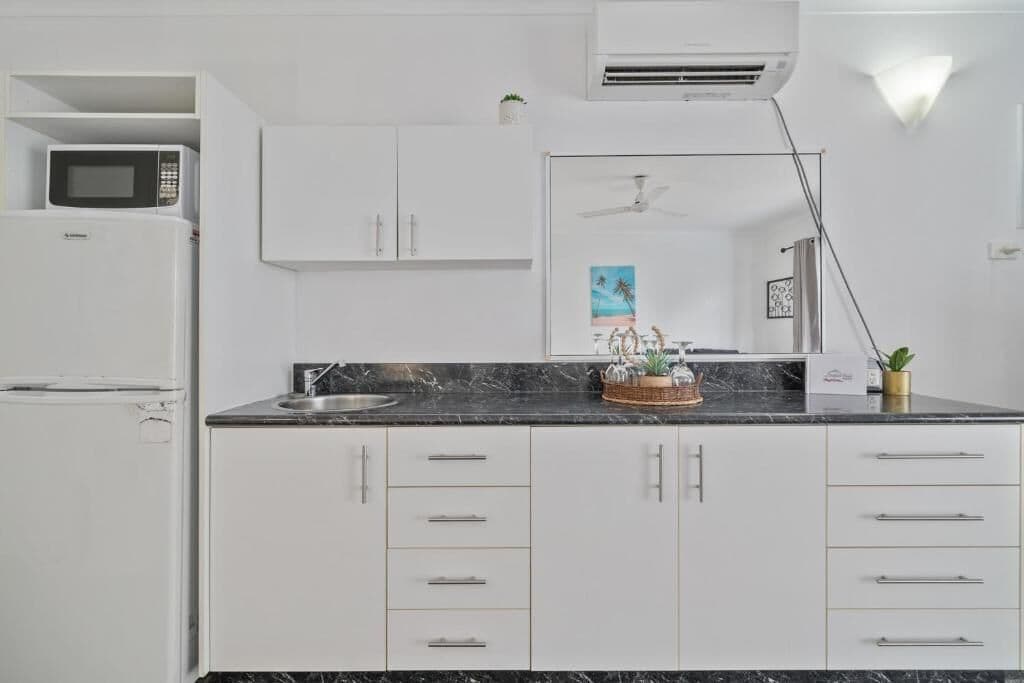 A modern kitchen with white cabinets, a black countertop, a microwave, and an air conditioning unit.