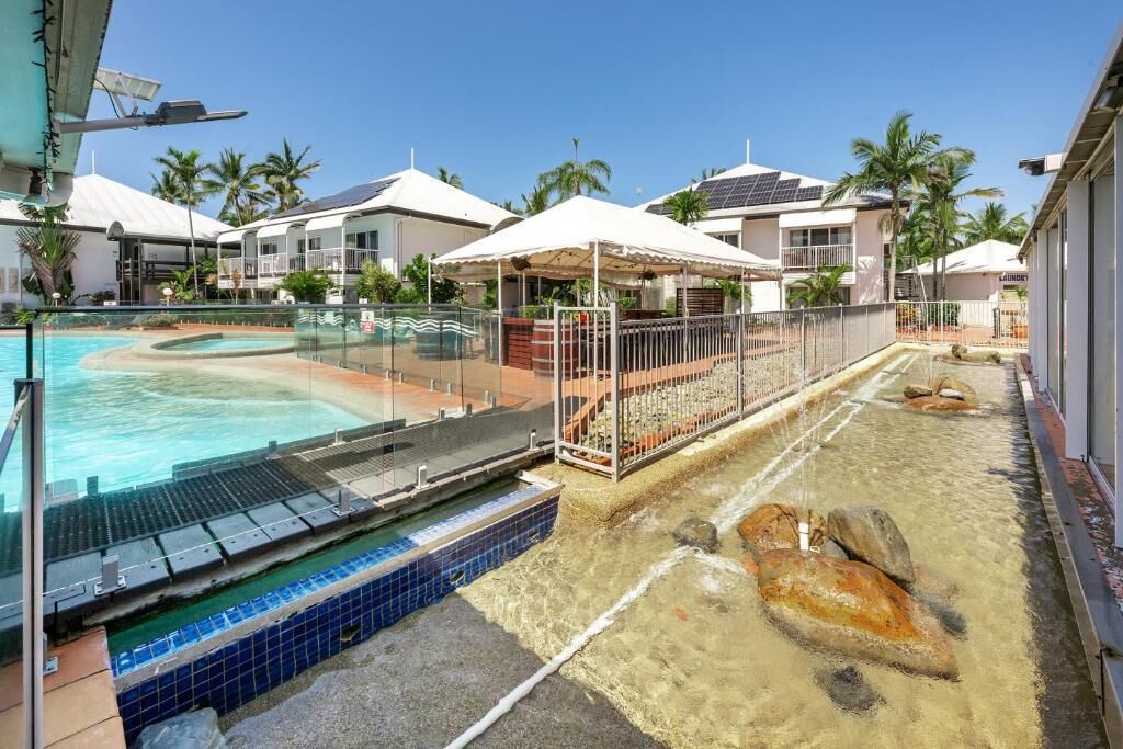 A swimming pool with a sunshade, a water feature, and a view of the surrounding buildings.