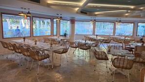 Un vaste espace dédié à la salle à manger, doté de grandes fenêtres, de chaises et de tables en osier, le tout mis en place pour les repas.