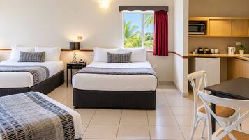 A hotel room with two beds, a small kitchenette, and a dining area.