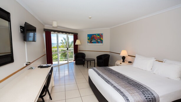 A hotel room with a bed, desk, chairs, a TV, and a painting.