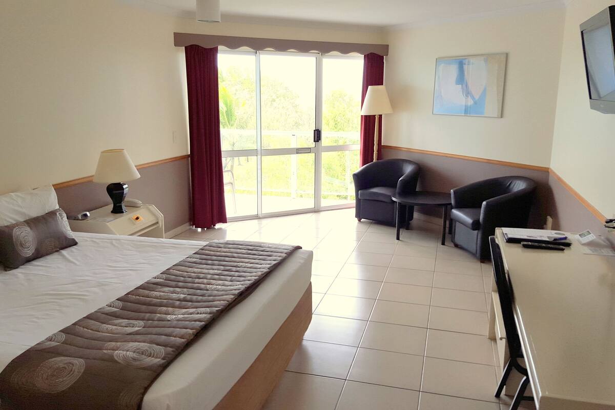 Une chambre d’hôtel avec un lit, un bureau, une chaise, une télévision et une fenêtre avec des rideaux.