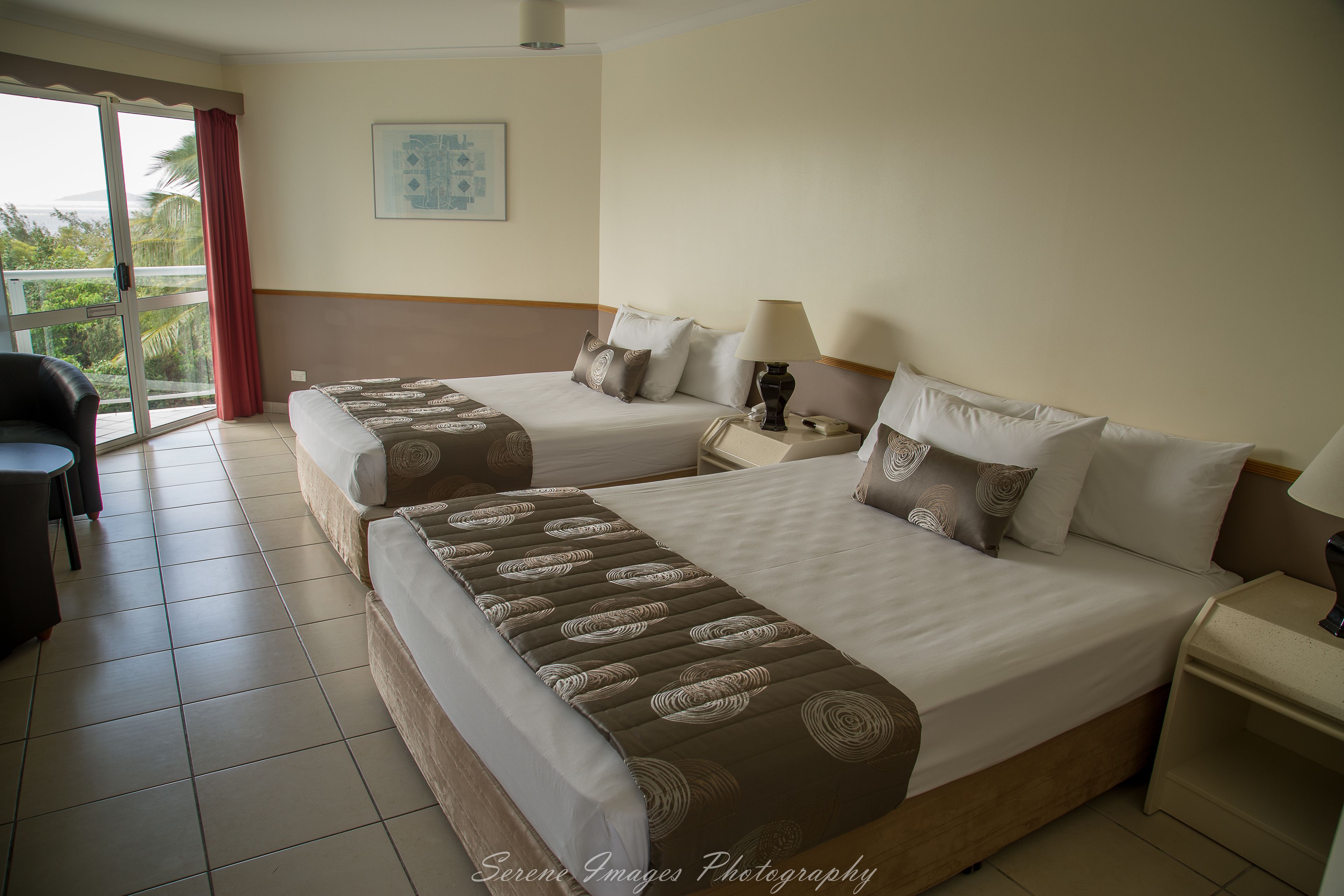 Une chambre d’hôtel avec deux lits, un bureau, une chaise et une vue sur l’extérieur.