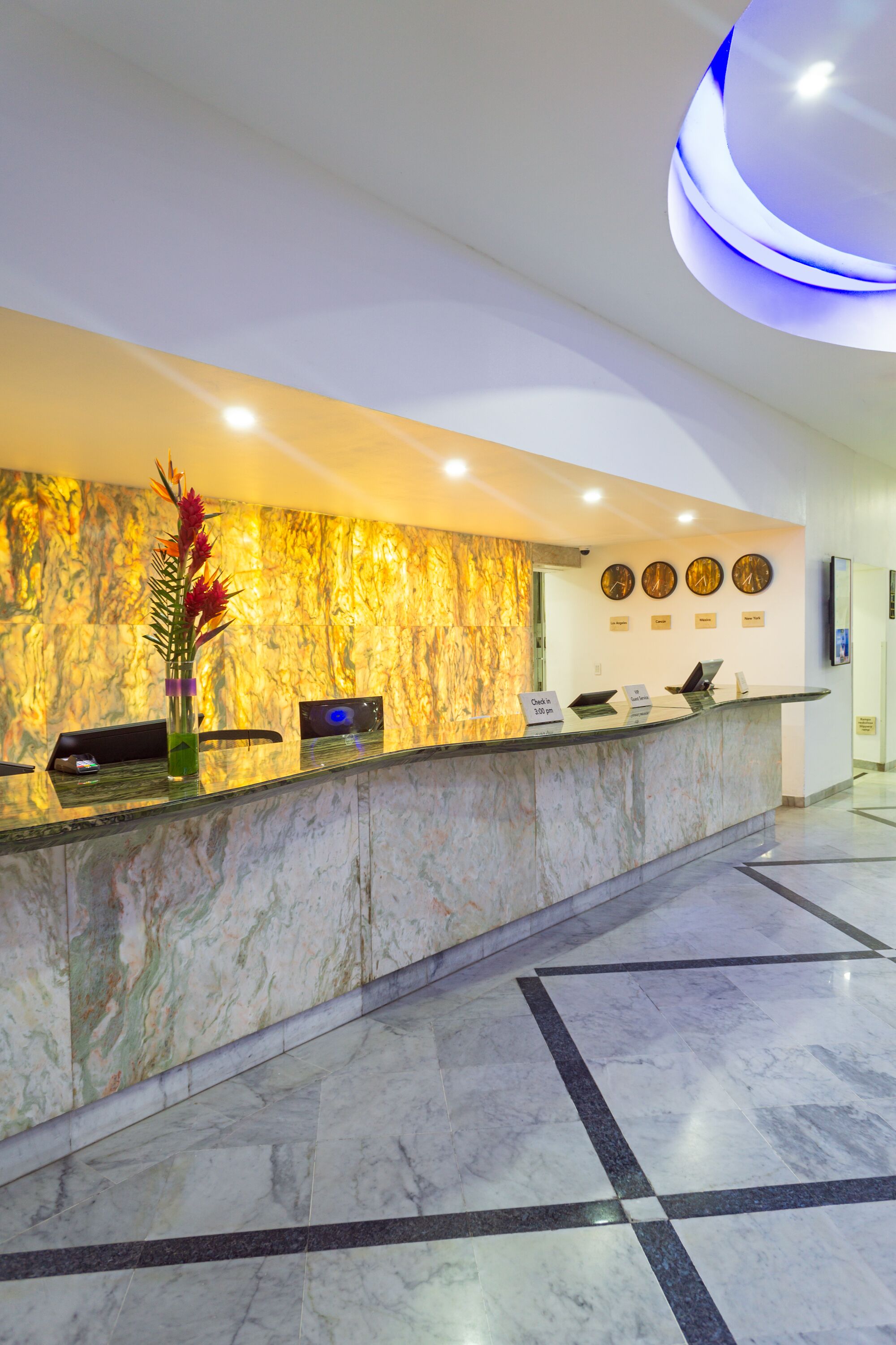 A hotel reception area with a marble counter, a vase with flowers, and a wall clock.