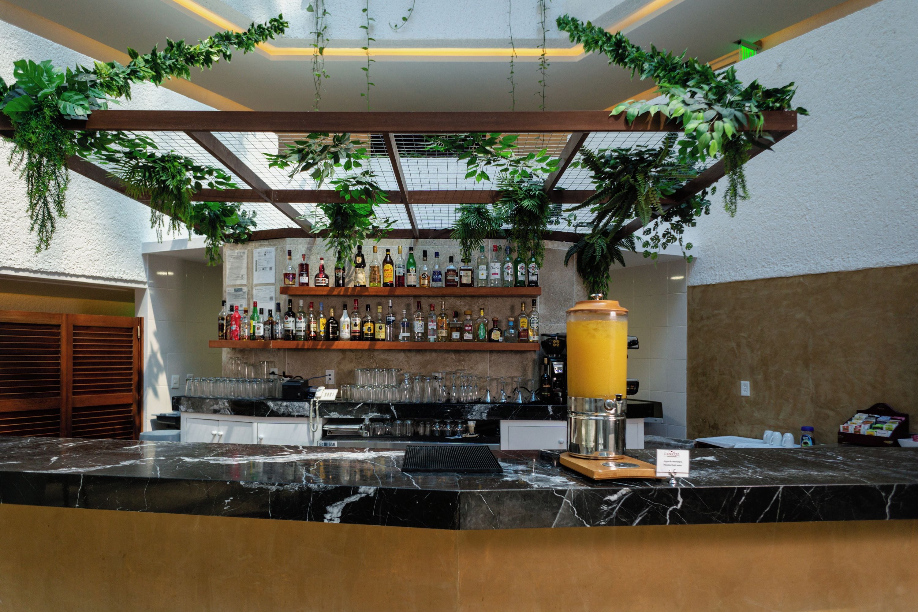 A bar area with a marble countertop, a variety of liquor bottles, and a large juice dispenser.