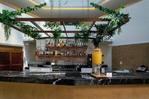 Zona de bar con encimera de mármol, varias botellas de licores y un dispensador grande de zumo.