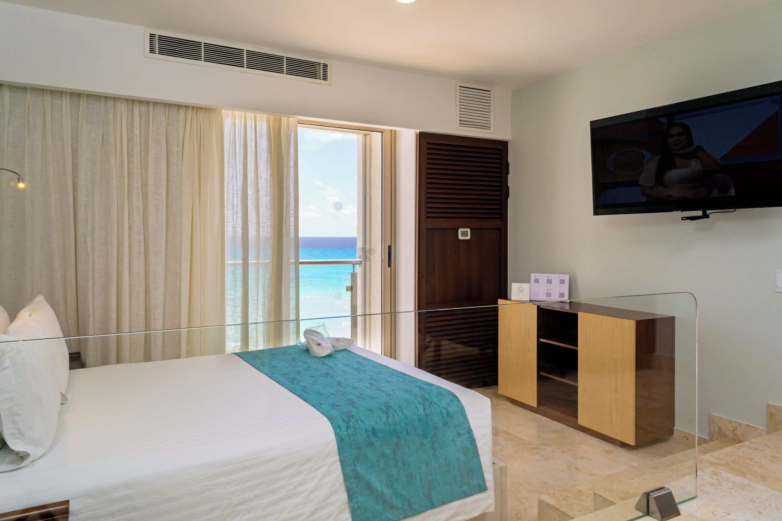 Habitación de hotel con cama, televisor, escritorio y vista al océano.