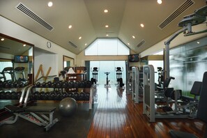 Et fitnessrum med forskellig træningsudstyr, en spejlvæg og et stort vindue.