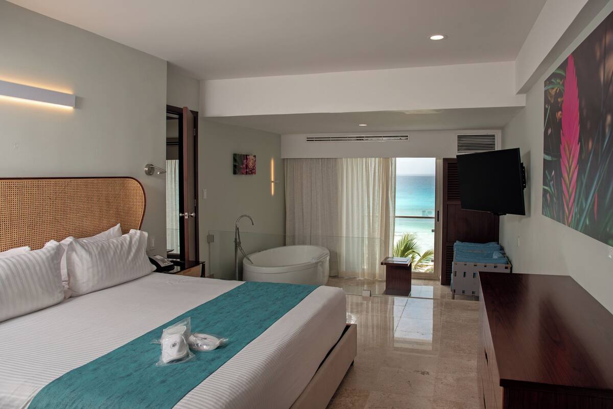 A hotel room with a bed, a bathtub, a TV, and a view of the ocean.