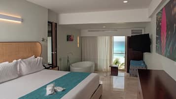 Habitación de hotel con cama, bañera, televisión y vista al océano.