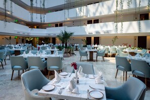 A spacious indoor dining area with multiple tables and chairs, featuring a modern design with hanging plants and a clean, white color scheme. - Sunset Royal Beach Resort - All Inclusive (Cancun)