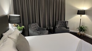 A hotel room with a large bed, two armchairs, a side table, a lamp, and a potted plant.