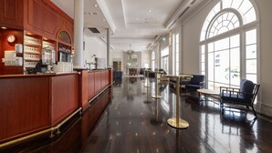 A spacious lobby with a polished wooden reception desk, seating area, and large arched windows.