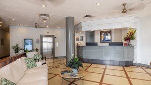 A hotel lobby with a reception desk, a waiting area with a sofa and coffee table, and a large pillar.