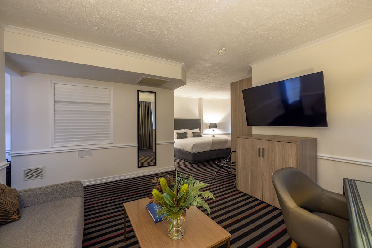 A hotel room with a bed, TV, sofa, and a table with a vase of flowers.