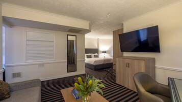 Quarto de hotel com cama, televisão, sofá e uma mesa com um vaso de flores.