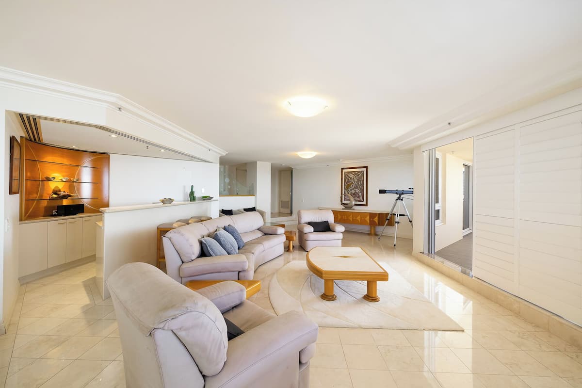 A spacious living area with a sofa set, a coffee table, and a side table. There is a wall-mounted shelf with decorative items and a telescope.
