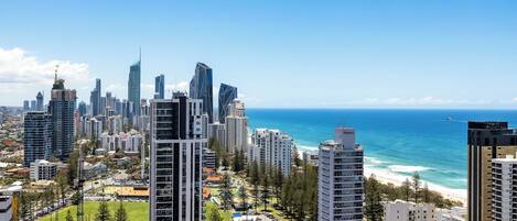 A coastal cityscape with high-rise buildings, a clear blue sky, and a beach in the distance.