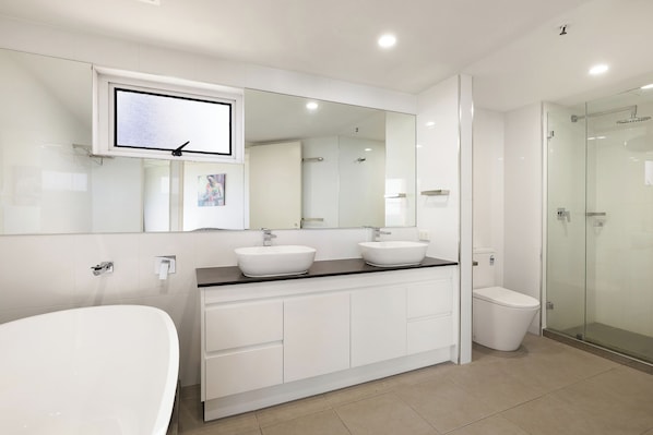 A modern bathroom with a large mirror, two sinks, a toilet, and a glass shower enclosure.