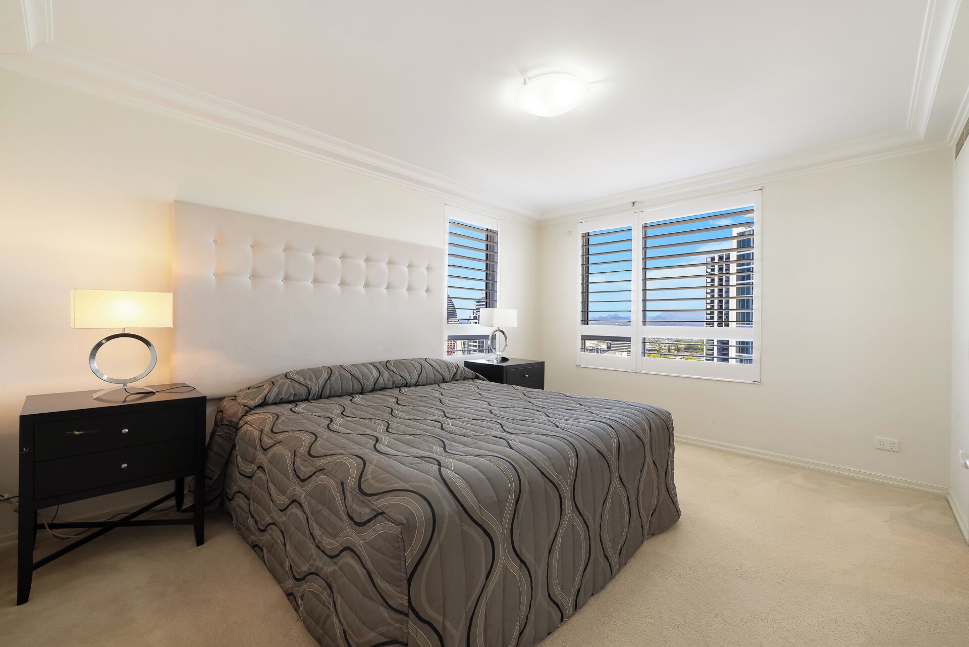 Une chambre à coucher avec un lit, une table de chevet avec une lampe, une commode et une fenêtre avec des stores.