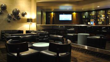 A bar area with a television screen, seating, and a bar stocked with various bottles.