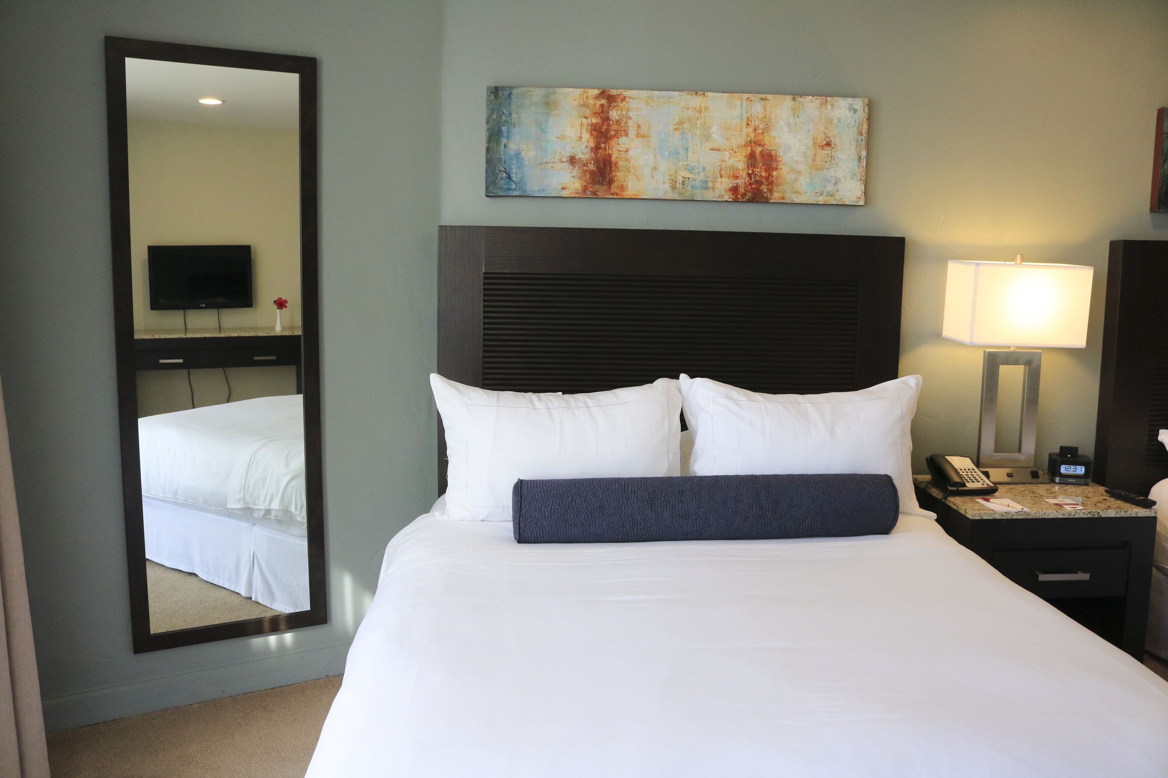 A hotel room with a large bed, a nightstand with a lamp, a telephone, and a painting on the wall.