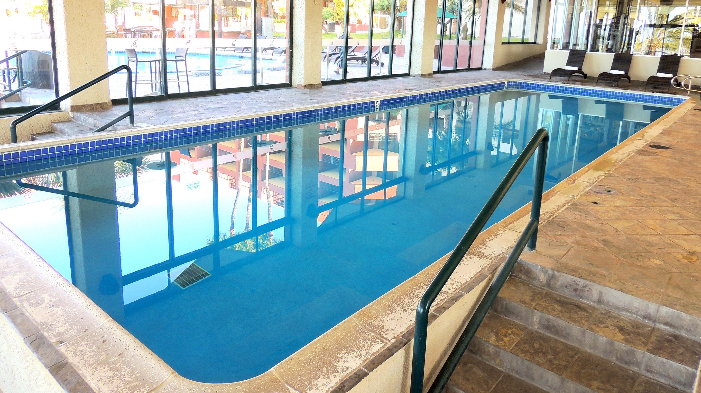 An indoor swimming pool with clear blue water, tiled edges, and a stone floor.