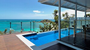 Piscina privada con barandilla de vidrio, con vista al mar azul cristalino y una isla rocosa.