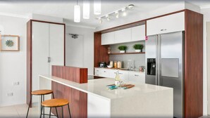 Una cocina moderna con armarios blancos, un refrigerador de acero inoxidable, una isla de madera y dos taburetes de bar.