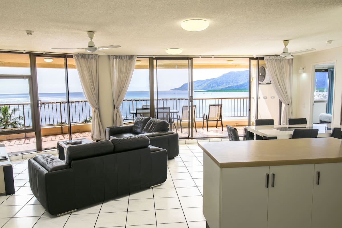 Un balcón amplio con sofá y zona de comedor, que ofrece vistas al mar y a las montañas.