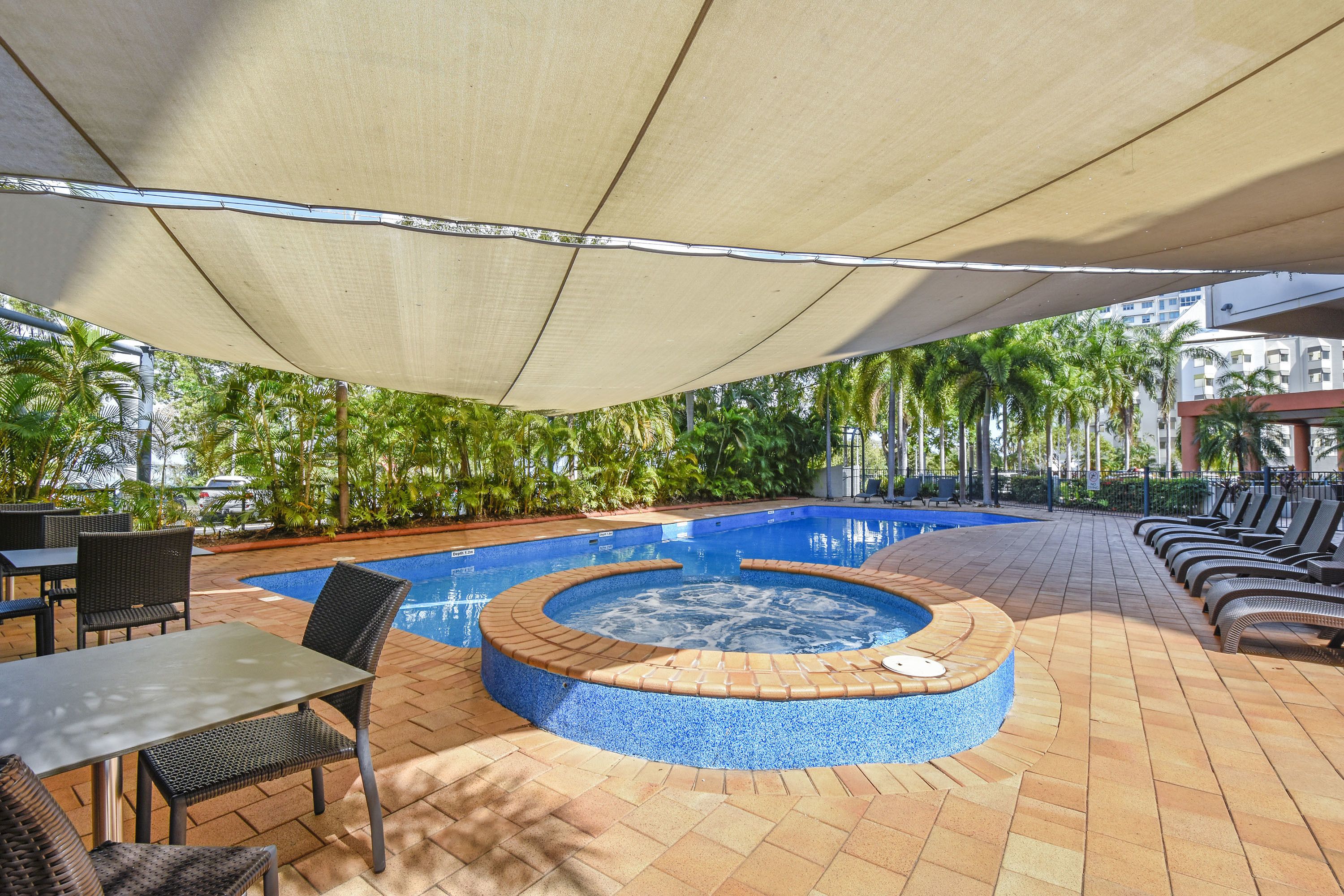 A pool area with a hot tub, lounge chairs, and tables under a canopy.
