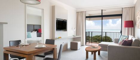 A modern hotel room with a dining area, a sofa, a TV, and a balcony with a view.