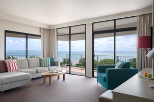 Una habitación de hotel moderna con balcón, sofá, mesa de centro y escritorio con lámpara.