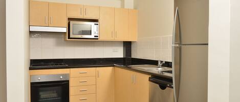 A compact kitchen with wooden cabinets, a built-in microwave, a stainless steel oven, and a refrigerator.