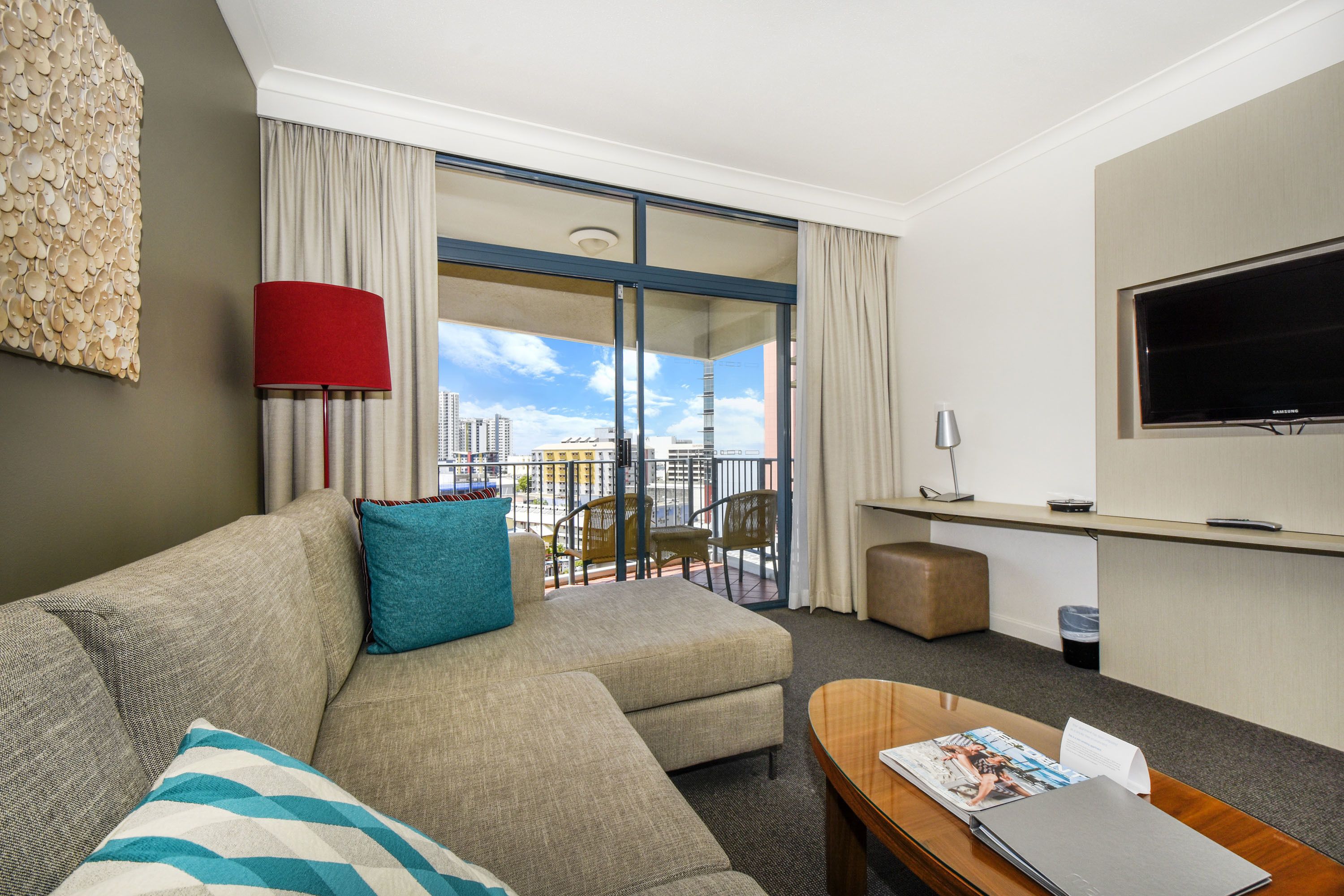 Habitación de hotel con sofá, mesa de centro, televisor, balcón con vistas y escritorio.