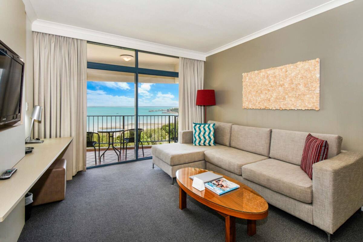 A hotel room with a balcony, a sofa, a coffee table, a TV, and a lamp.