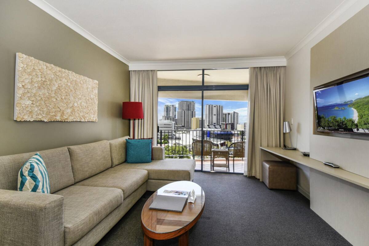 A hotel room with a sofa, a coffee table, a TV, and a balcony with a city view.