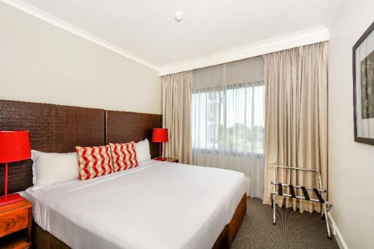 A hotel room with a large bed, two bedside tables with lamps, a window with curtains, and a headboard.